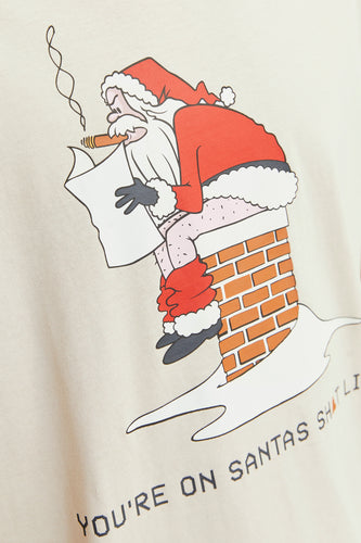 Beige T-shirt met een cartoon van de Kerstman die een sigaar rookt en uit een schoorsteen komt, met de tekst "You're on Santa's Sh*t List".
