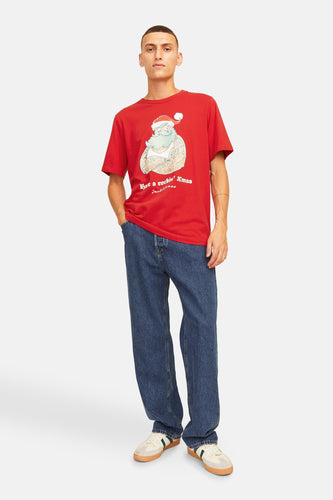 Man met rood T-shirt met kerstmotief, blauwe jeans en witte sneakers.