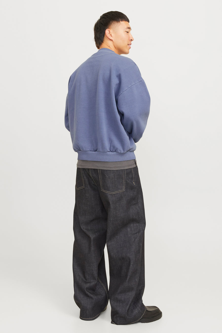 Een man met een blauwe trui en wijde, donkere jeans.