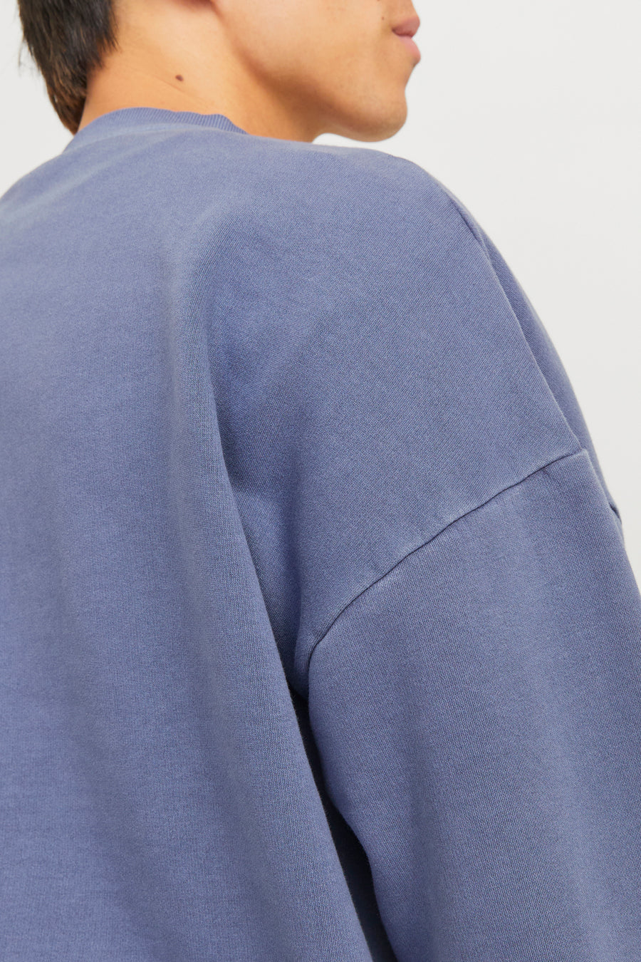 Close-up van de schouder en een gedeelte van het gezicht van een persoon met een blauw-paarse trui.