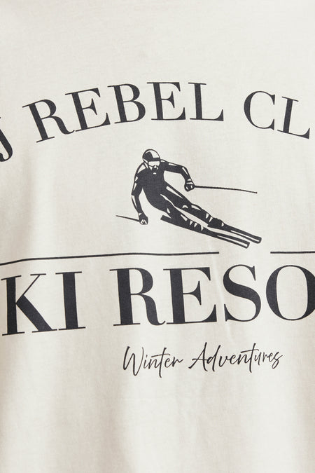 T-shirt beige à manches courtes de JJREBEL, avec une impression noire d'un skieur et du texte.