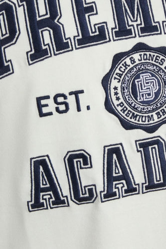 Close-up van een wit kledingstuk met marineblauwe geborduurde tekst en een logo met de tekst "JACK & JONES".