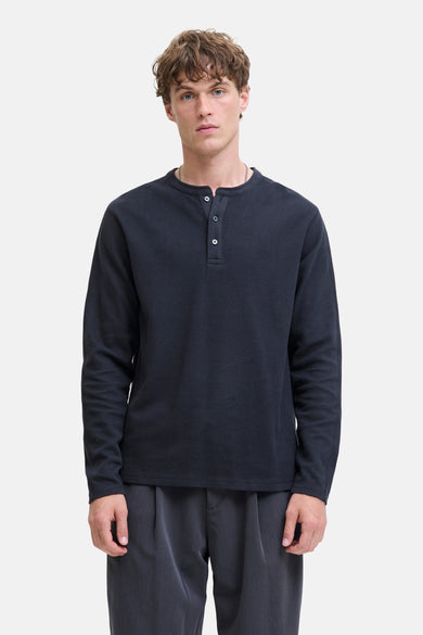 T-shirt bleu marine à manches longues de PREMIUM BLUE par JACK & JONES, avec fermeture à boutons et porté avec un pantalon gris.