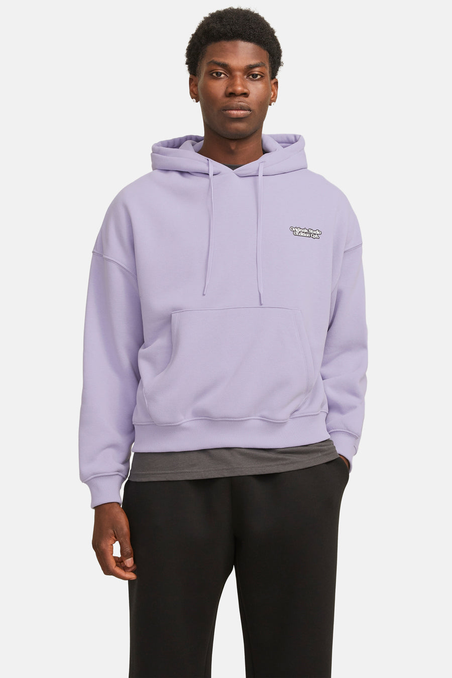 Een staande man draagt een lila hoodie en een zwarte broek.