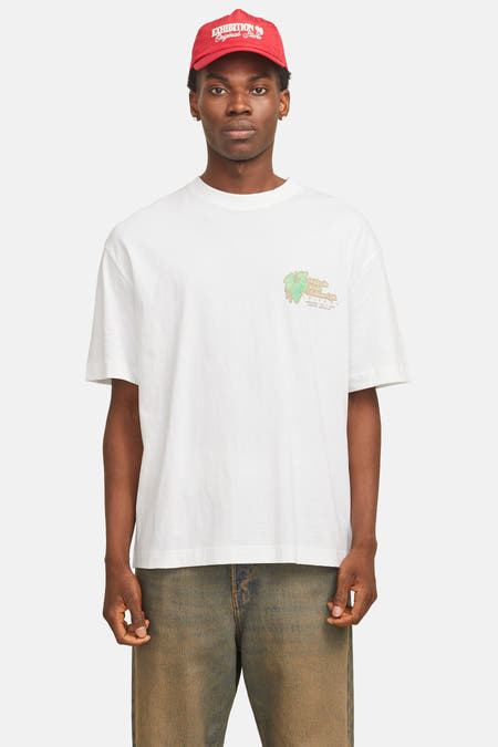 T-shirt blanc à manches courtes d'ORIGINALS BY JACK & JONES, avec une petite impression sur la poitrine, associé à un chapeau rouge et des jeans foncés.
