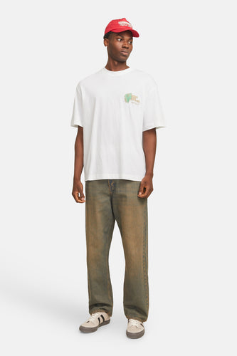 Een man in een wit t-shirt, verweerde jeans, sneakers en een rode pet.