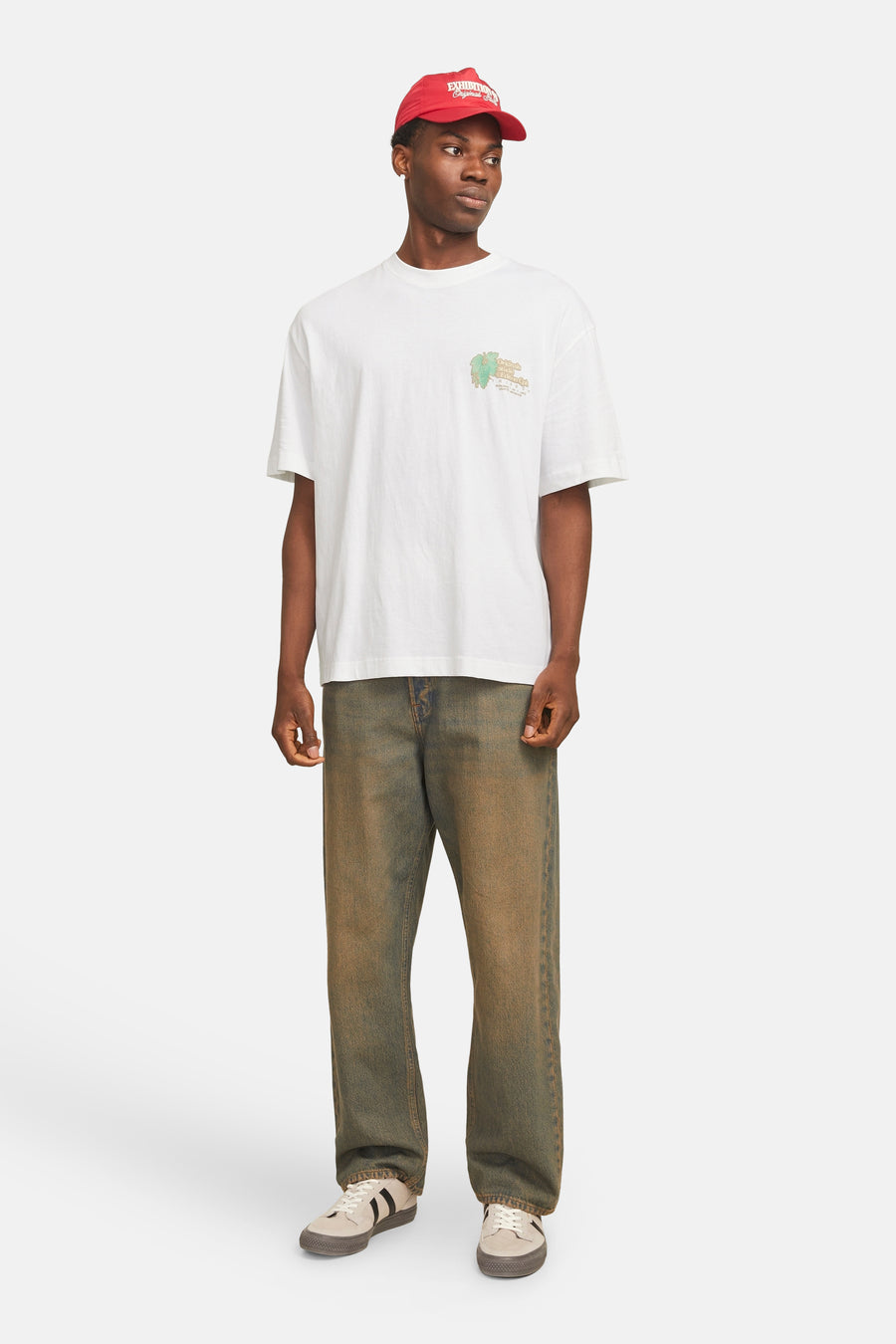 Een man in een wit t-shirt, verweerde jeans, sneakers en een rode pet.