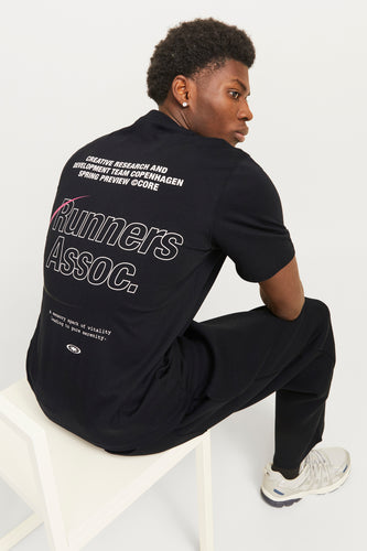 Zittende man met zwart T-shirt met witte opdruk en grijze sneakers.