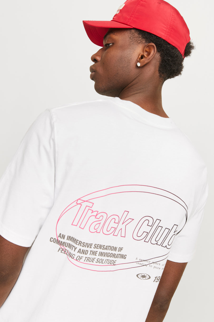 Portret van een man met een rode pet en een wit T-shirt met 'Track Club'-opdruk.