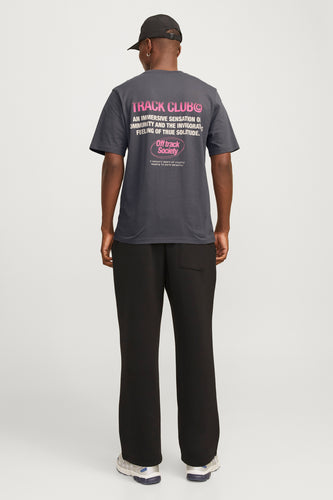 Een man van achteren in een grijze T-shirt met roze tekst, zwarte broek en een zwarte pet.