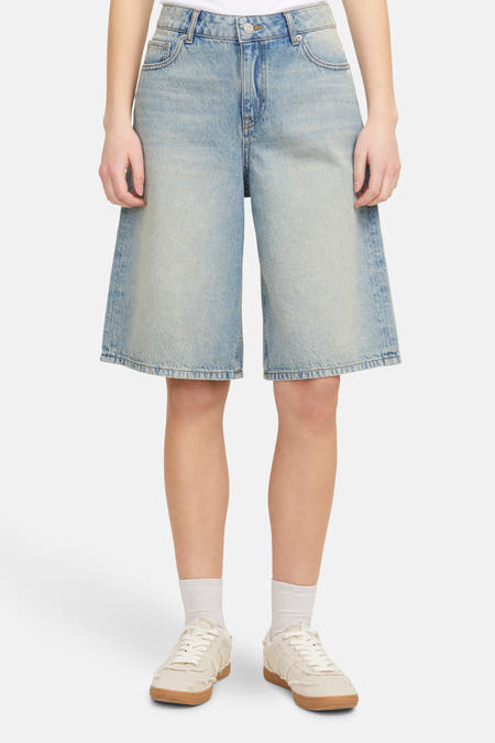 Short de denim bleu clair de JJXX, avec des jambes larges et associé à des chaussettes blanches et des baskets crème.