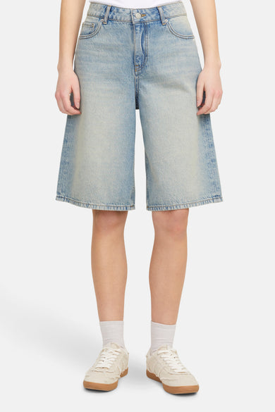 Short de denim bleu clair de JJXX, avec des jambes larges et associé à des chaussettes blanches et des baskets crème.