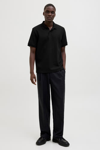 Polo noir à manches courtes de CORE BY JACK & JONES, avec une subtile texture et porté avec un pantalon et des chaussures en cuir.