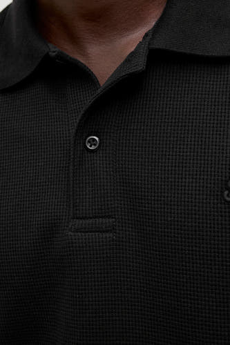 Polo noir à manches courtes de CORE BY JACK & JONES, avec une subtile texture rayée et une fermeture à boutons.