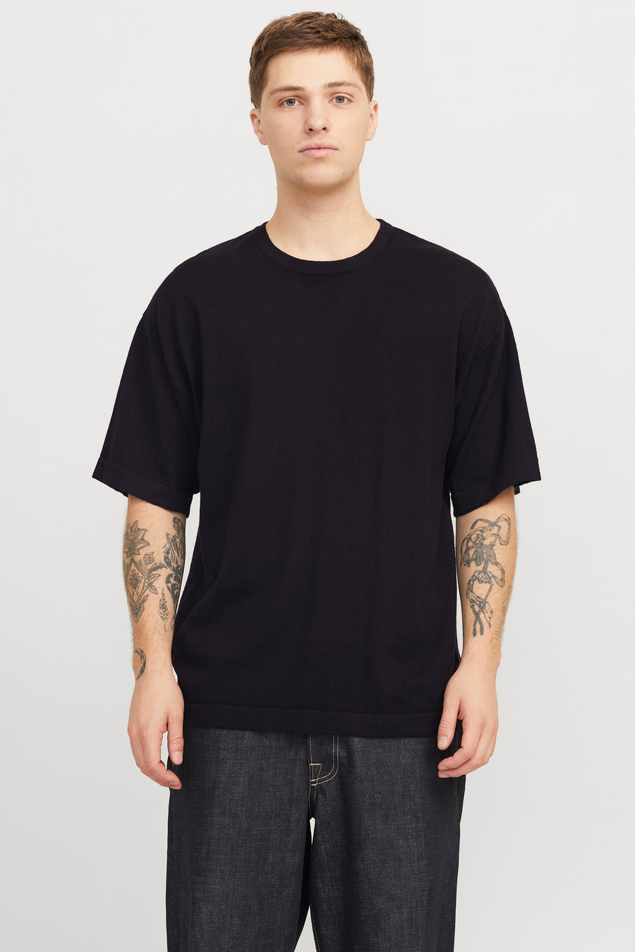 T-shirt noir à manches courtes de PREMIUM by JACK & JONES, avec des tatouages sur les deux bras, associé à un jean foncé.