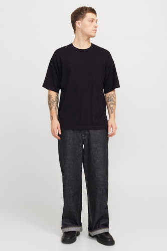 T-shirt noir à manches courtes de PREMIUM by JACK & JONES, avec des tatouages sur les bras, associé à des jeans bleu marine et des chaussures noires.