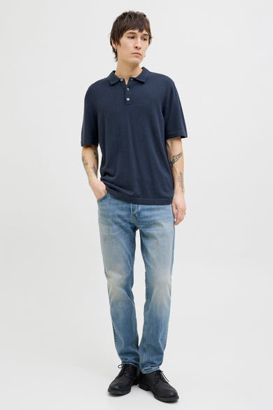 Man in blauw poloshirt en jeans, staand.
