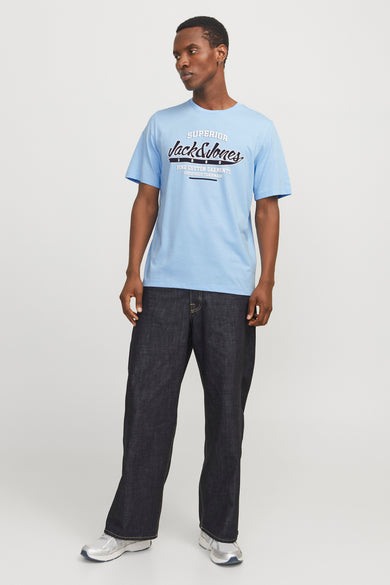 T-shirt bleu à manches courtes de JACK & JONES, avec impression textuelle sur la partie avant, associé à des jeans foncés et des baskets argentées.