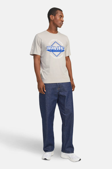 T-shirt écru à manches courtes d'ORIGINALS par JACK & JONES, avec une impression bleue et associé à des jeans et des baskets.