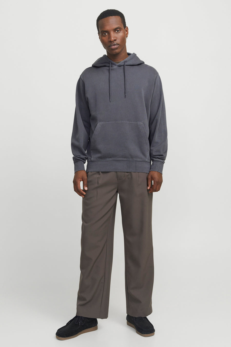 Sweat à capuche gris de CORE BY JACK & JONES avec cordons de serrage et poche kangourou, porté par un mannequin avec un pantalon ample marron et des chaussures en daim noires.