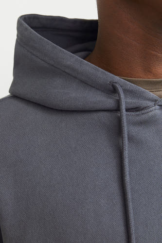 Gros plan d'un sweat à capuche gris de CORE BY JACK & JONES avec une texture côtelée fine, des cordons de serrage et un t-shirt vert olive.