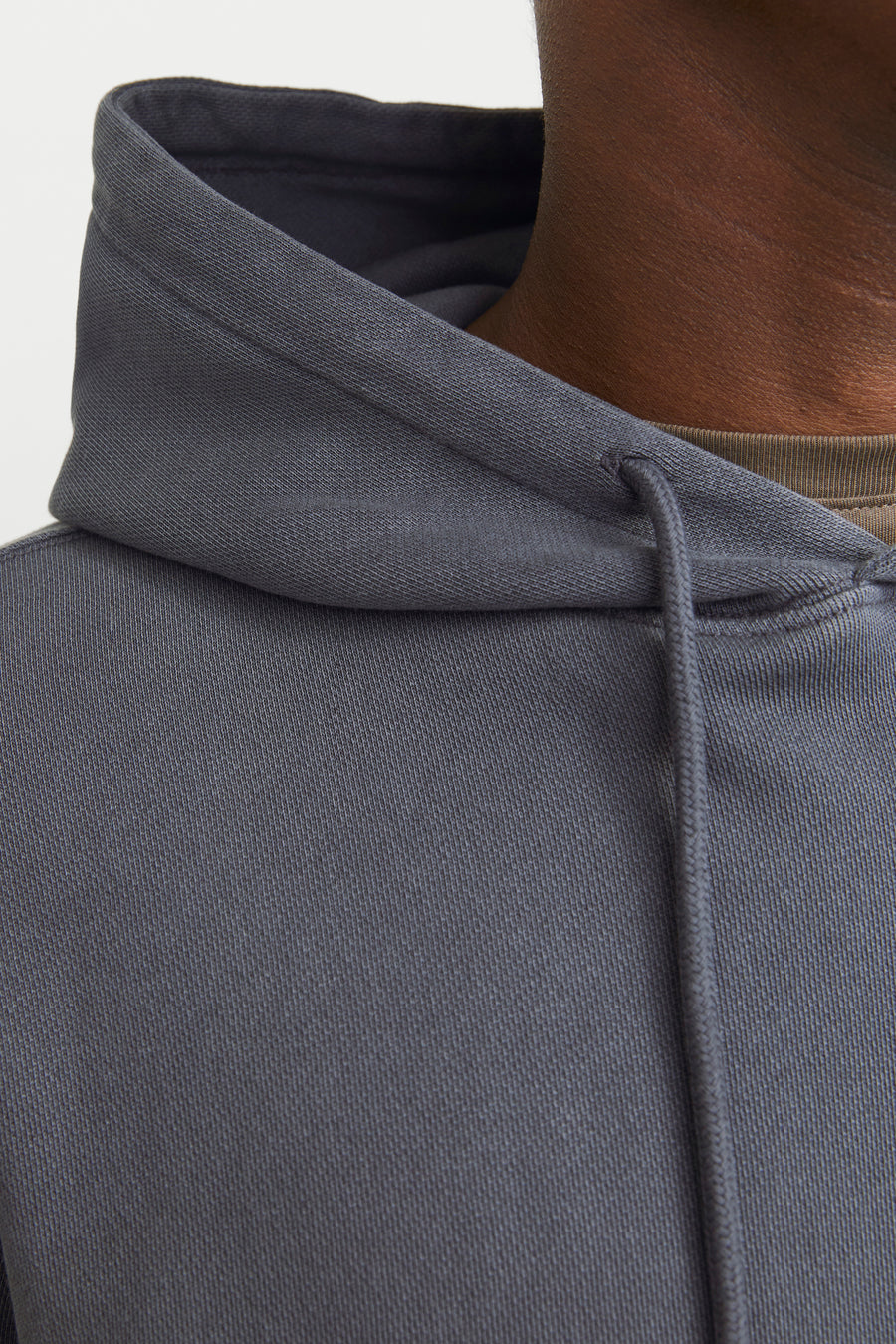 Gros plan d'un sweat à capuche gris de CORE BY JACK & JONES avec une texture côtelée fine, des cordons de serrage et un t-shirt vert olive.