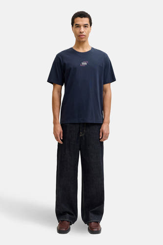 Blauw T-shirt met korte mouwen van CORE by JACK & JONES, met een logo op de borst, gedragen met wijde jeans en bruine schoenen.
