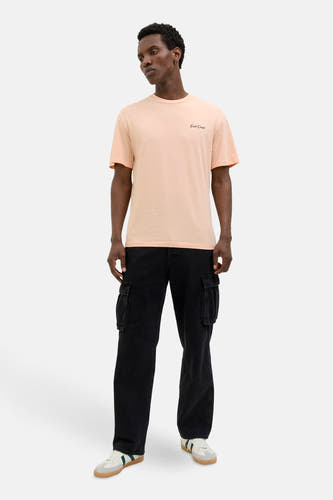 Oranje T-shirt met korte mouwen van ORIGINALS BY JACK & JONES, met kleine zwarte tekst, gecombineerd met zwarte broek en witte sneakers.
