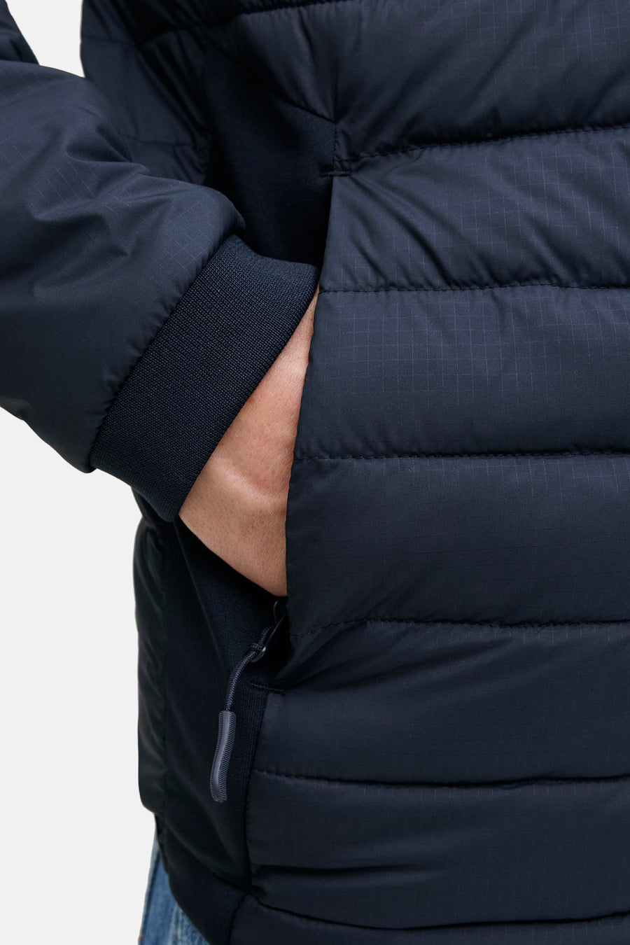 Donkerblauwe gewatteerde jas met geribbelde manchetten en hand in zak.
