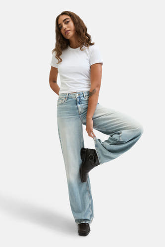 Jean bleu clair large de JJXX, associé à un t-shirt blanc et des bottes noires dans une pose décontractée.