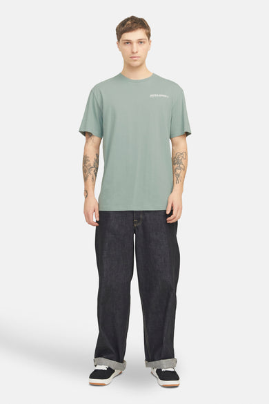 T-shirt vert de mantes man cour Originals Jack par Jack & &, avec un petit logo sur la poitrine, associé à des jeans foncés et des baskets.