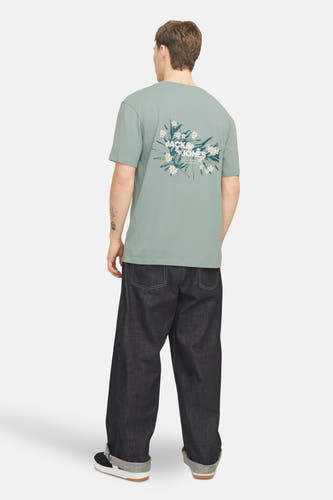 T-shirt vert de man mantes coursSSSSSS & J J, dé avec un détail floral sur le dos, associé à des jeans larges et foncés.