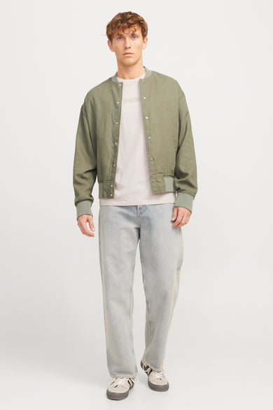 T-shirt écru à manches courtes de CORE BY JACK & JONES, porté sous un blouson kaki et des jeans bleu clair.