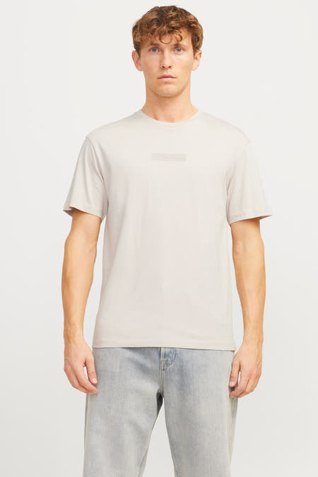 T-shirt écru à manches courtes de CORE BY JACK & JONES, avec un logo subtil sur la poitrine et porté avec des jeans bleus.