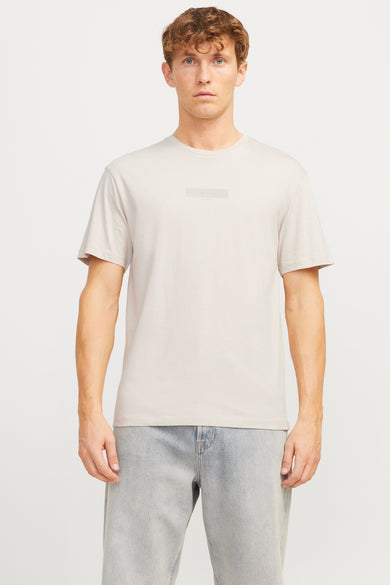T-shirt écru à manches courtes de CORE BY JACK & JONES, avec un logo subtil sur la poitrine et porté avec des jeans bleus.
