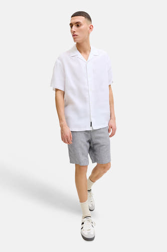Short bleu de JACK & JONES JEANS INTELLIGENCE avec une texture tissée, porté par un homme en chemise blanche et baskets.
