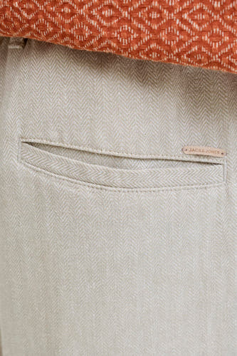 Gros plan d'un short beige JACK & JONES JEANS INTELLIGENCE à motif chevrons, avec une poche arrière et une étiquette de marque marron, stylisé avec un haut en maille orange.