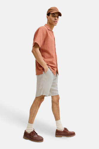 Short beige de JACK & JONES JEANS INTELLIGENCE avec texture subtile, porté par un homme avec une chemise orange et des chaussures marron.