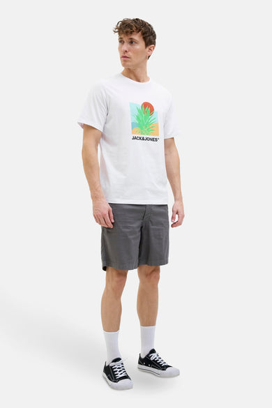 T-shirt blanc à manches courtes d'ORIGINALS BY JACK & JONES, avec une impression graphique et associé à des shorts gris, des chaussettes blanches et des baskets noires.