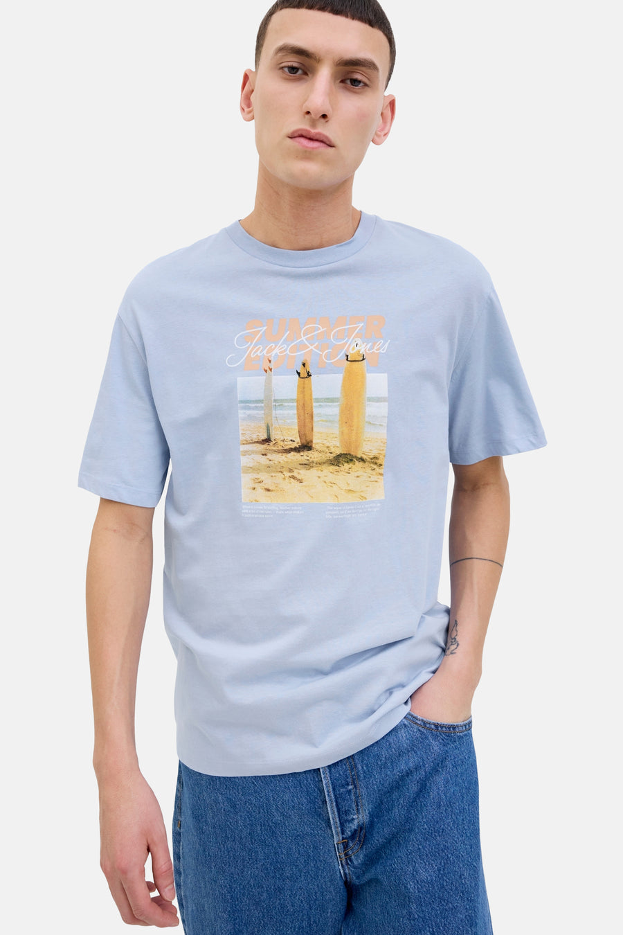 T-shirt bleu à manches courtes d'ORIGINALS BY JACK & JONES, avec une image de plage sur l'avant, porté avec des jeans.
