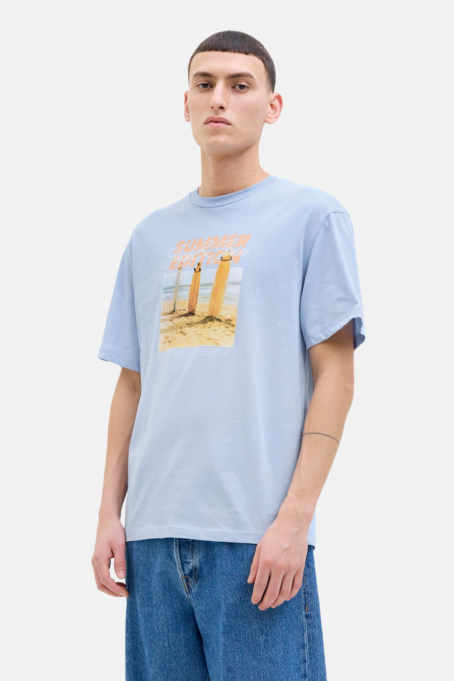 T-shirt bleu à manches courtes d'ORIGINALS BY JACK & JONES, avec une impression estivale de plage et porté avec un jean bleu.