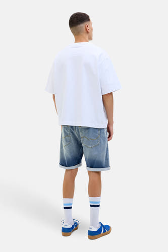 Jean court en denim bleu de JACK & JONES JEANS INTELLIGENCE, avec des poches rabattues et associé à un T-shirt blanc et des baskets bleues.