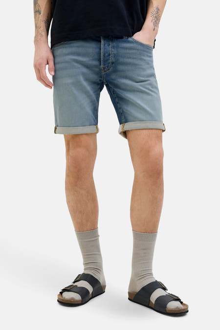 Jean court en denim bleu marine de JACK & JONES JEANS INTELLIGENCE, avec des poches rabattues et des chaussettes grises et des sandales.