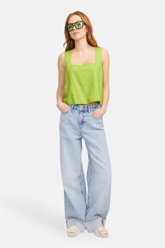 Vrouw in groene top en wijde jeans, met handen in zakken.