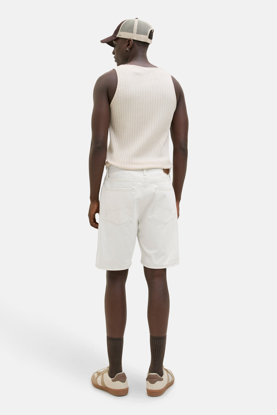 Man van achteren in een mouwloze top, witte korte broek en sneakers.