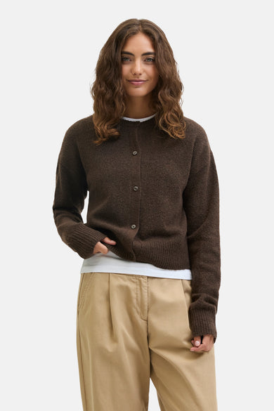 Veste brune de JJXX, portée sur un chemisier blanc, avec un pantalon plissé beige et des chaussures marron foncé.