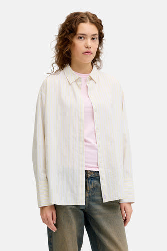 Chemise rayée jaune (manches longues) de JJXX, portée sur une chemise rose, avec des jeans bleu marine et des chaussures marron.