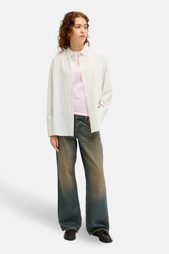 Geel gestreept overhemd (lange mouwen) van JJXX, gedragen over een roze shirt, met donkerblauwe jeans en bruine schoenen.
