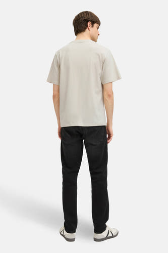 Beige T-shirt met korte mouwen van JJREBEL, met een effen kleur en gecombineerd met zwarte jeans en sportschoenen.
