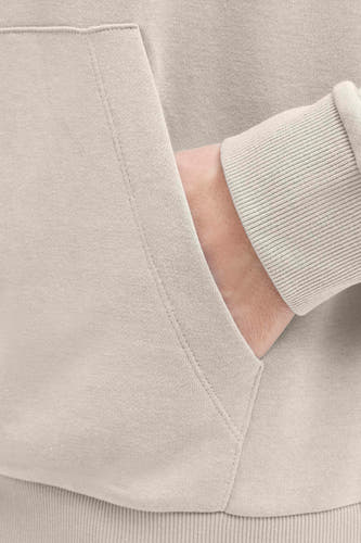 Pull beige à capuche JJREBEL, avec une main dans la poche, texture douce et poignets côtelés.